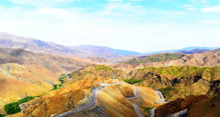 Route alpine élevée serpentant à travers les montagnes de l'Atlas accidentées et multicolores sous un ciel lumineux.