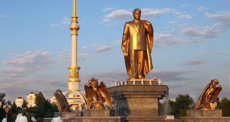 Golden statue of Turkmenistan’s leader stands before the soaring Ashgabat Monument in evening light.