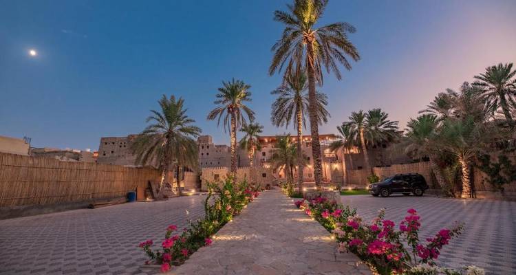 Allée bordée de palmiers menant à une structure traditionnelle semblable à un fort sous le clair de lune.