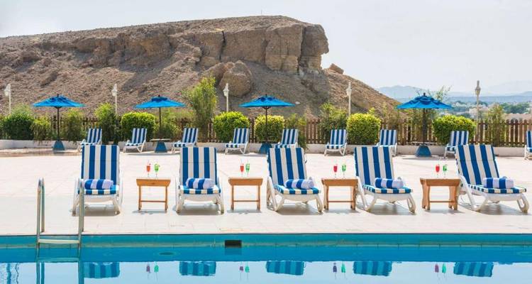 Piscine extérieure avec des chaises longues à rayures bleues et une colline rocheuse en arrière-plan.