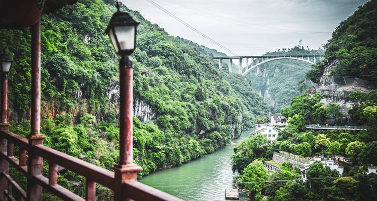 Paisaje de garganta verde visto desde un balcón con un puente arqueado a la distancia.