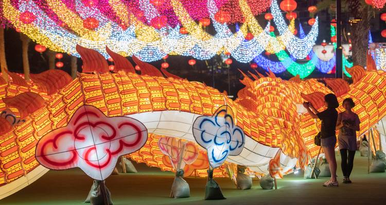 Los visitantes fotografían una enorme linterna de dragón iluminada rodeada de luces de festival coloridas por la noche.