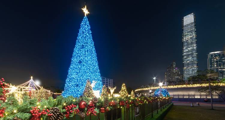 Un enorme árbol de Navidad azul brilla junto al horizonte de Hong Kong bajo un cielo nocturno oscuro.