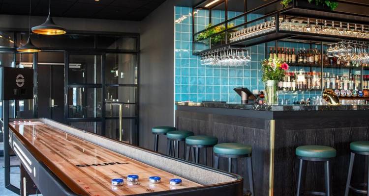 Bar moderne avec une table de shuffleboard et des murs carrelés bleus.