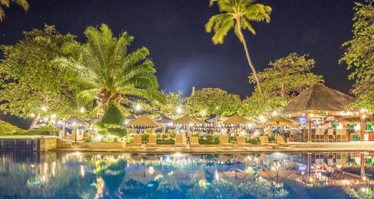 Nighttime view of a pool area with lit palm trees and umbrellas.