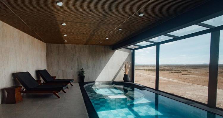 Área de piscina cubierta con tumbonas y vista al exterior.