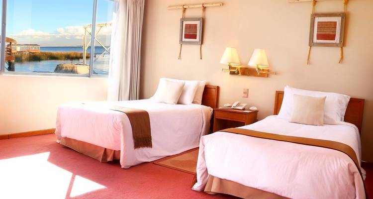 Bright hotel room with twin beds and a view of a lakeside.