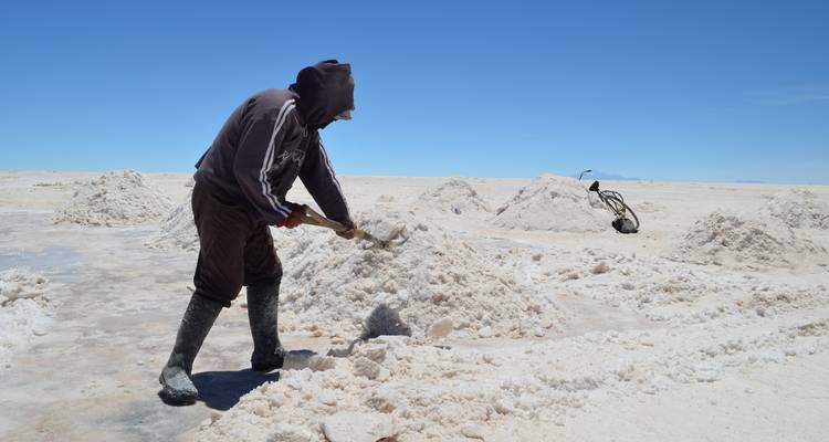 Worker harvesting salt flats with piles of salt in the background.
