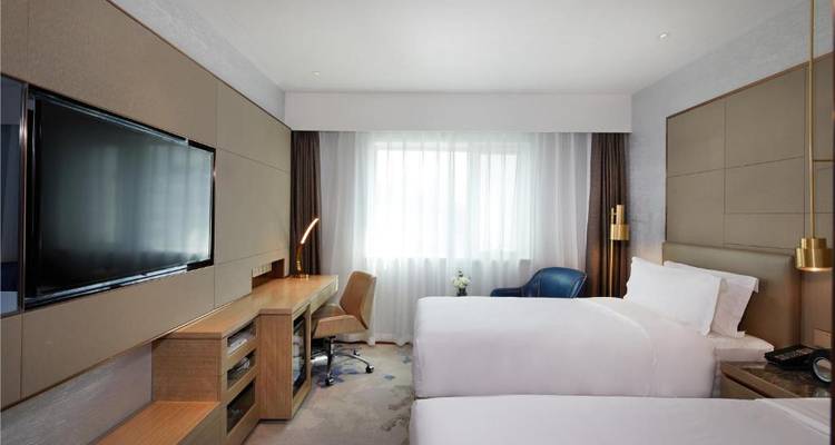 Twee eenpersoonsbedden in een moderne hotelkamer met een tv en werkbureau.