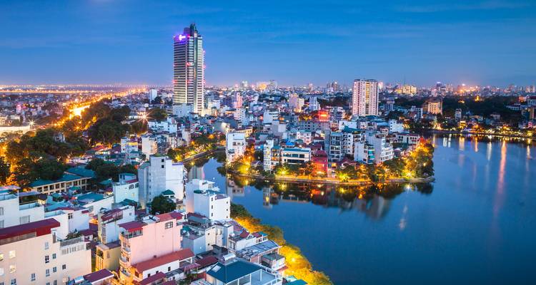 Een stadsgezicht met verlichte gebouwen en een rivier tijdens de avond.