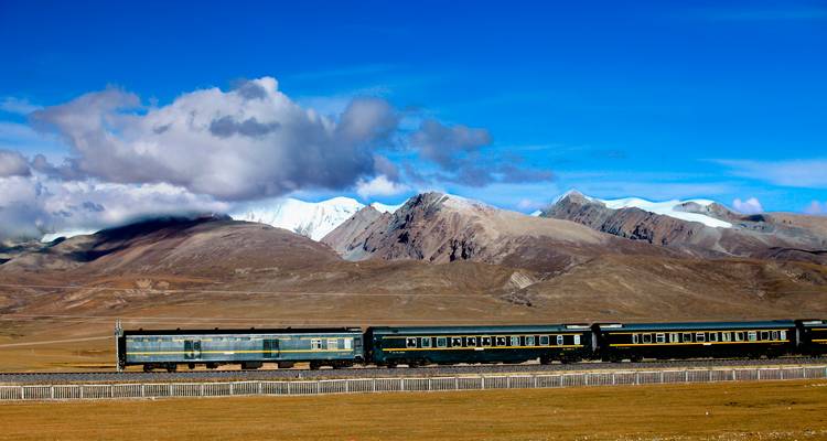 Una vista panorámica de un tren viajando a través de una cordillera con cumbres nevadas.