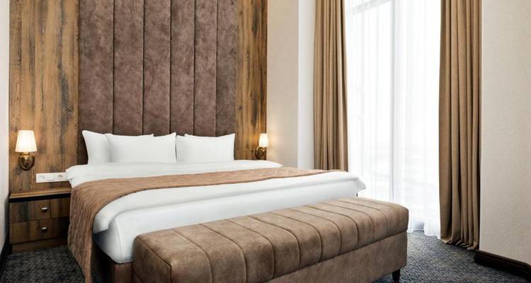 Hotelzimmer mit einem großen Bett, gepolsterter Bank und natürlichem Licht durch die Vorhänge.