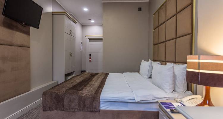 Innenraum eines modernen Hotelzimmers mit Bett, Fernseher und neutraler Dekoration.