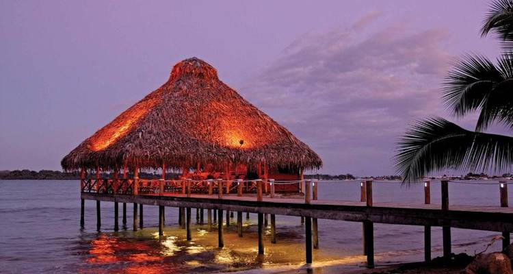 Hutte au toit de chaume au-dessus de l'océan illuminée la nuit.