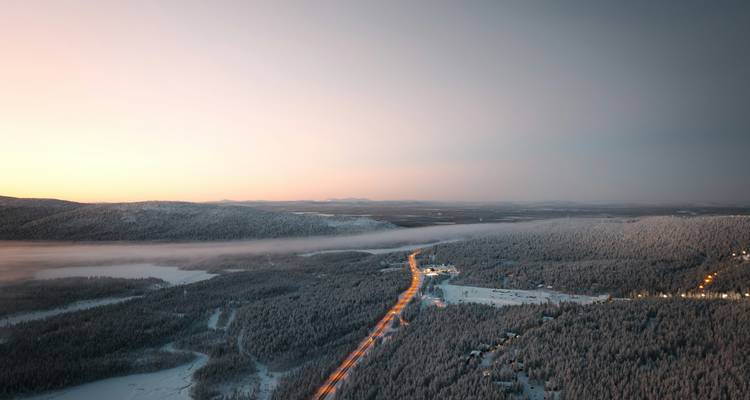 Een lange weg loopt door een met sneeuw bedekt boslandschap in de schemering.