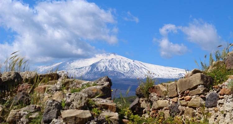 L'Etna enneigé visible derrière un premier plan rocheux.
