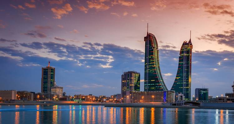 Twin towers reflected in water with a city skyline at dusk.