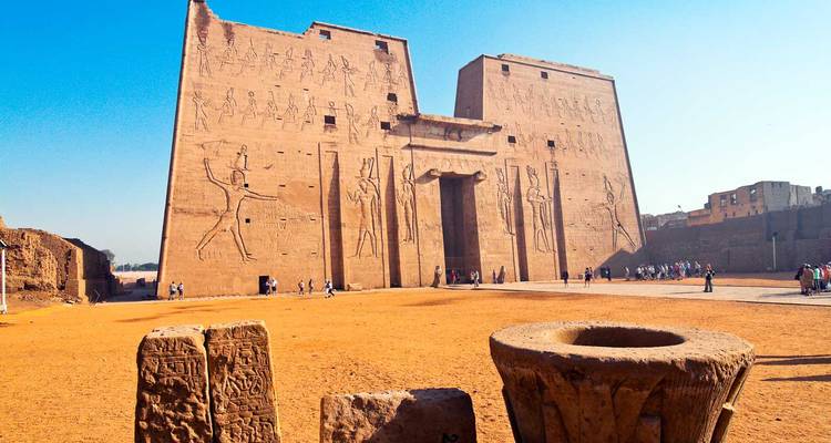 Templo del antiguo Egipto con grabados y turistas cerca.