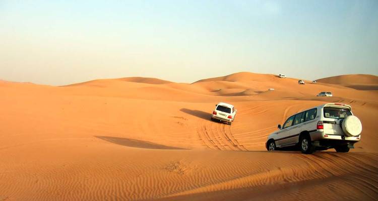 Woestijnlandschap met auto's die over zandduinen rijden.