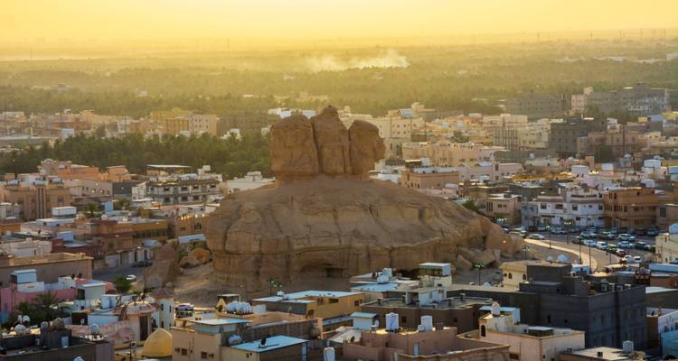 Formación rocosa única con vista a un pueblo al atardecer.