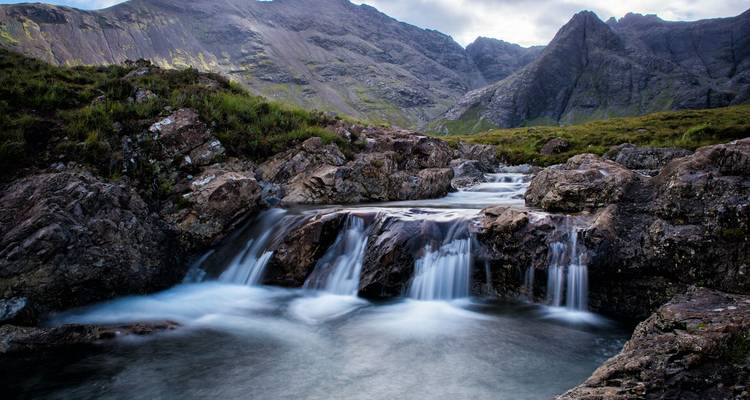 Une petite cascade sur des rochers avec des montagnes en arrière-plan.