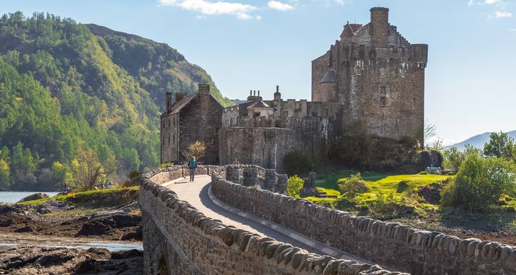 Un château historique avec un pont pittoresque et des montagnes en arrière-plan.