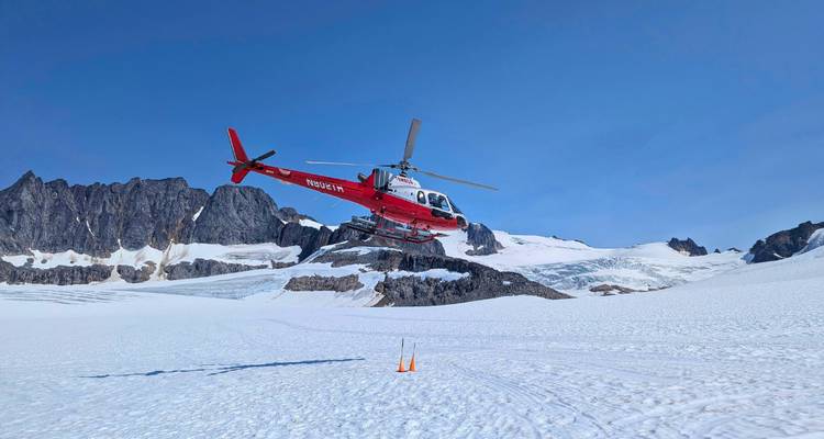 Hélicoptère rouge volant au-dessus d'un paysage montagneux enneigé.