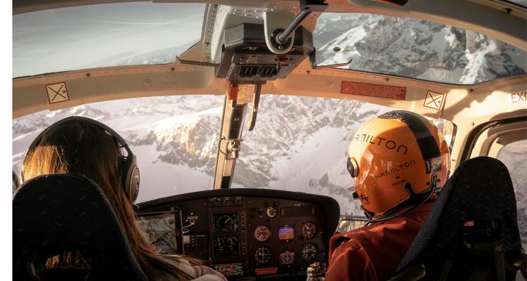 Vue depuis le cockpit d'un hélicoptère survolant des montagnes enneigées.