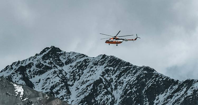 Hélicoptère volant près d'un sommet montagneux escarpé couvert de neige.