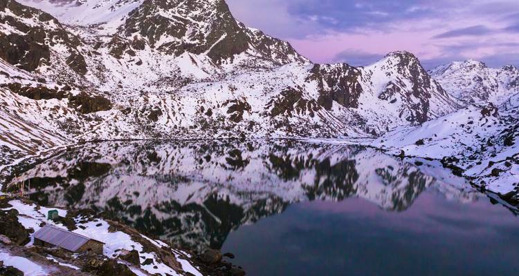 Snow-covered mountains reflecting in a calm lake at dawn