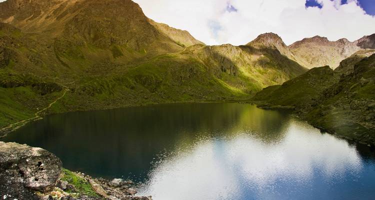 Mountain lake reflecting surrounding peaks under a partly cloudy sky.