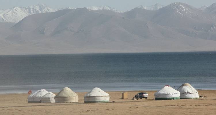 Yourtes au bord d'un lac avec des montagnes au loin.