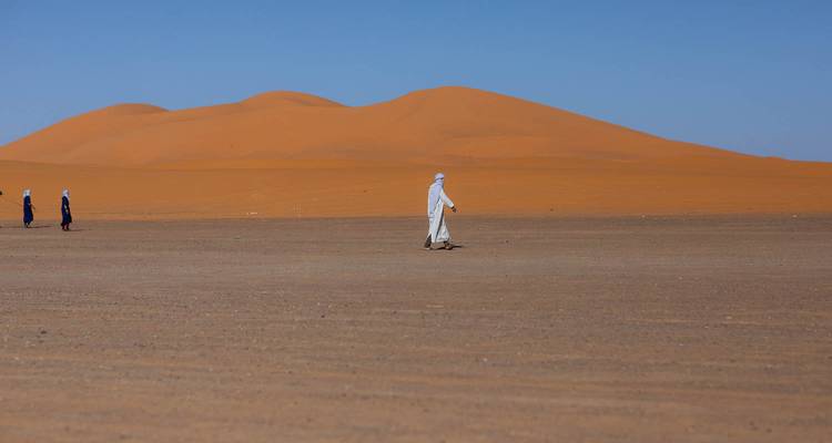 Des gens marchant à travers un vaste paysage désertique plat.