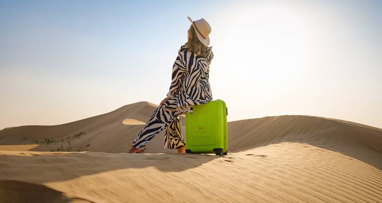 Une femme avec une valise posant en tenue de désert sur des dunes de sable.