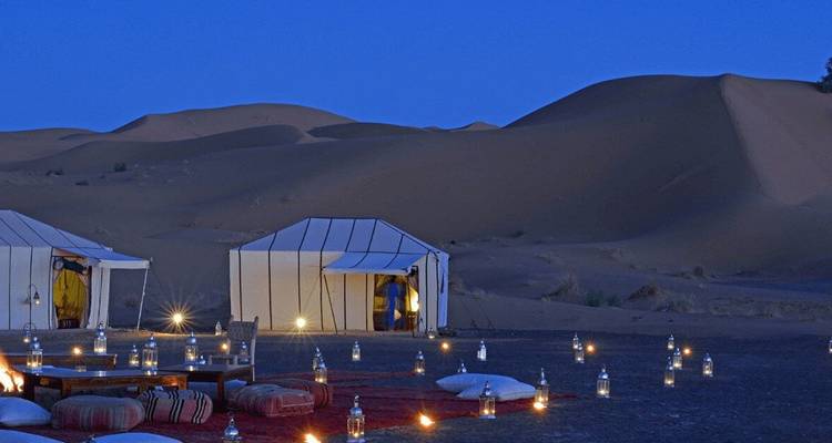 Un camp du désert la nuit avec des tentes et des lanternes illuminées.