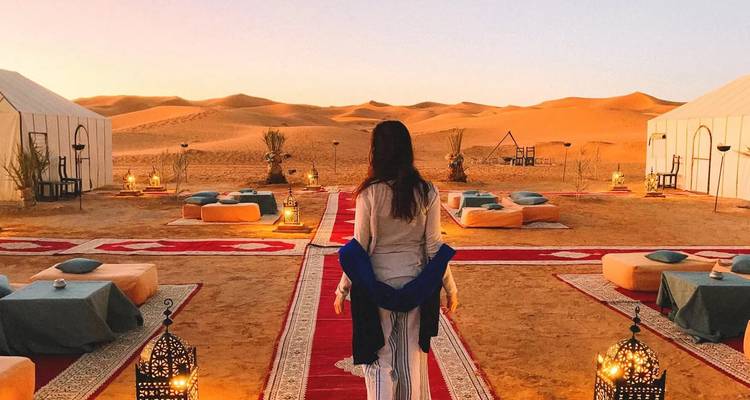 Personne marchant vers un campement dans le désert au crépuscule.