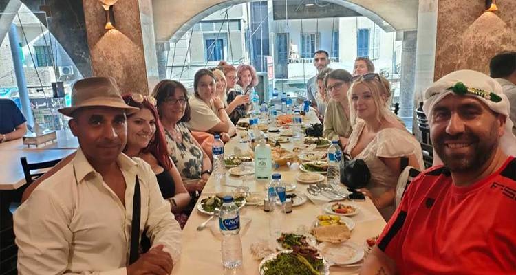 Grand groupe de personnes dînant à de longues tables à l'intérieur.