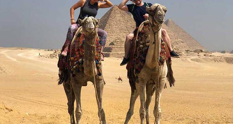 Des gens à dos de chameaux dans le désert près des pyramides.