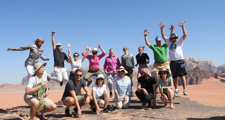Grupo de personas saltando en una cornisa rocosa en un paisaje desértico.