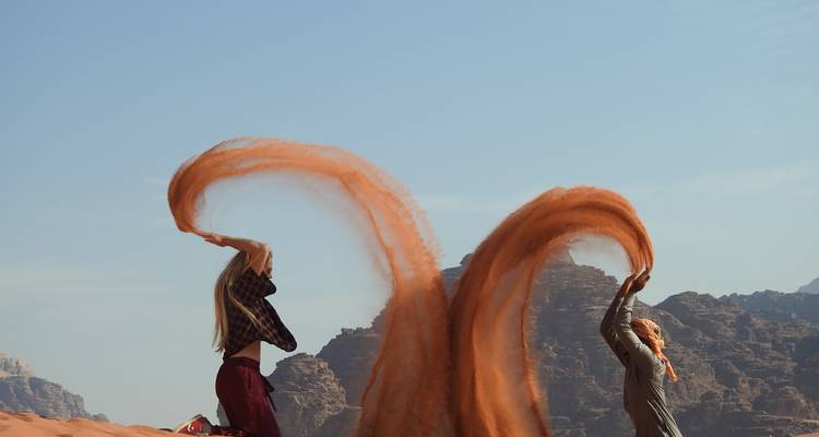 Mujeres jugando con arena en un desierto con formaciones rocosas.