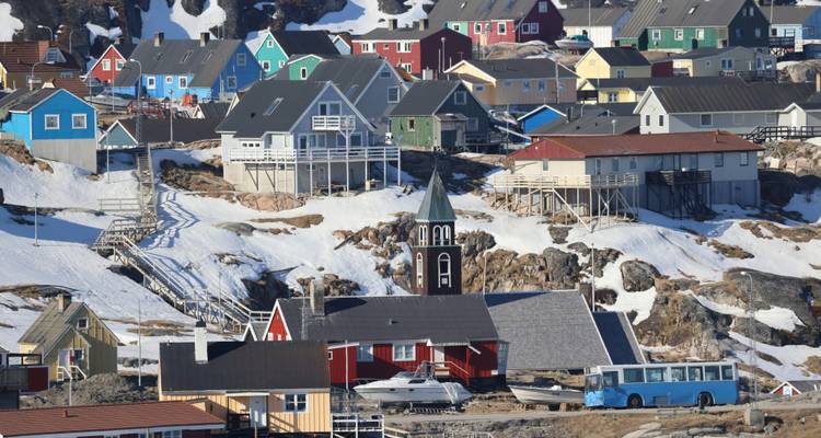 Colorful houses on a snowy hillside in Greenland with a small church.