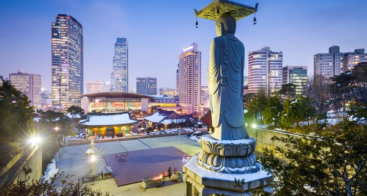Statue overlooking a modern cityscape at twilight.