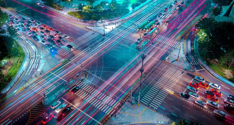 Vista aérea nocturna de una intersección urbana concurrida con estelas de luz de los vehículos.