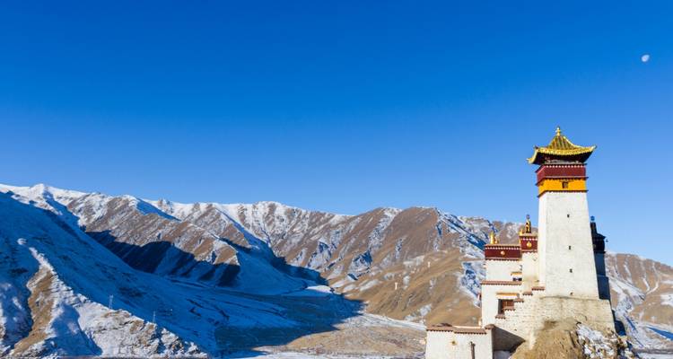 Ein entfernter Turm auf einem Hügel mit schneebedeckten Bergen dahinter.
