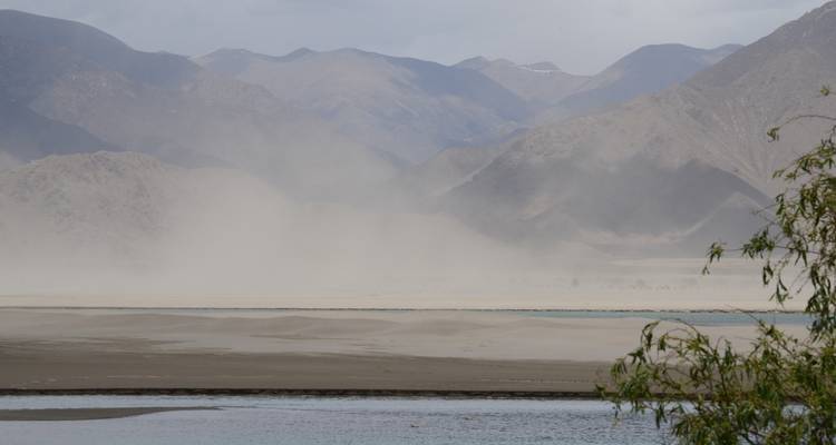 Staubiges Tal mit entfernten geschichteten Bergen unter einem dunsigen Himmel.