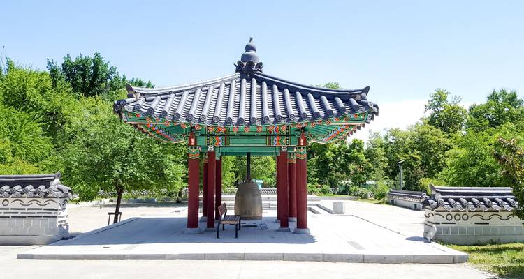 Traditioneel Koreaans paviljoen met een bel, omringd door groen.