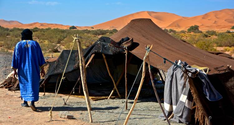 Personne en robe bleue marchant vers une structure de tente dans le désert.