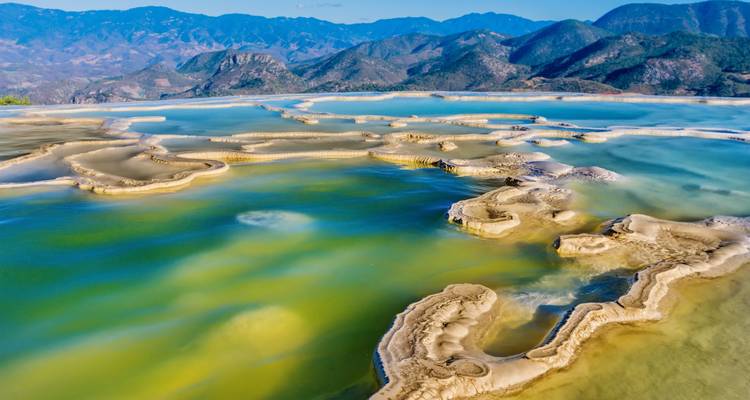 Luftaufnahme der terrassenförmigen Mineralpools von Hierve el Agua mit Bergen im Hintergrund