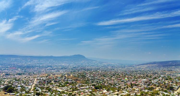 Panoramisch luchtbeeld over een uitgestrekte stad in een vallei met verre bergen onder gestreepte blauwe luchten