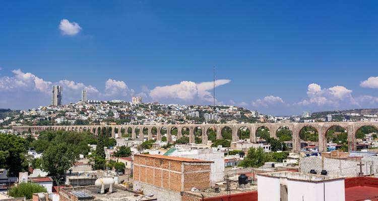 Largos arcos de piedra del acueducto se extienden a través de Querétaro bajo un cielo azul intenso.